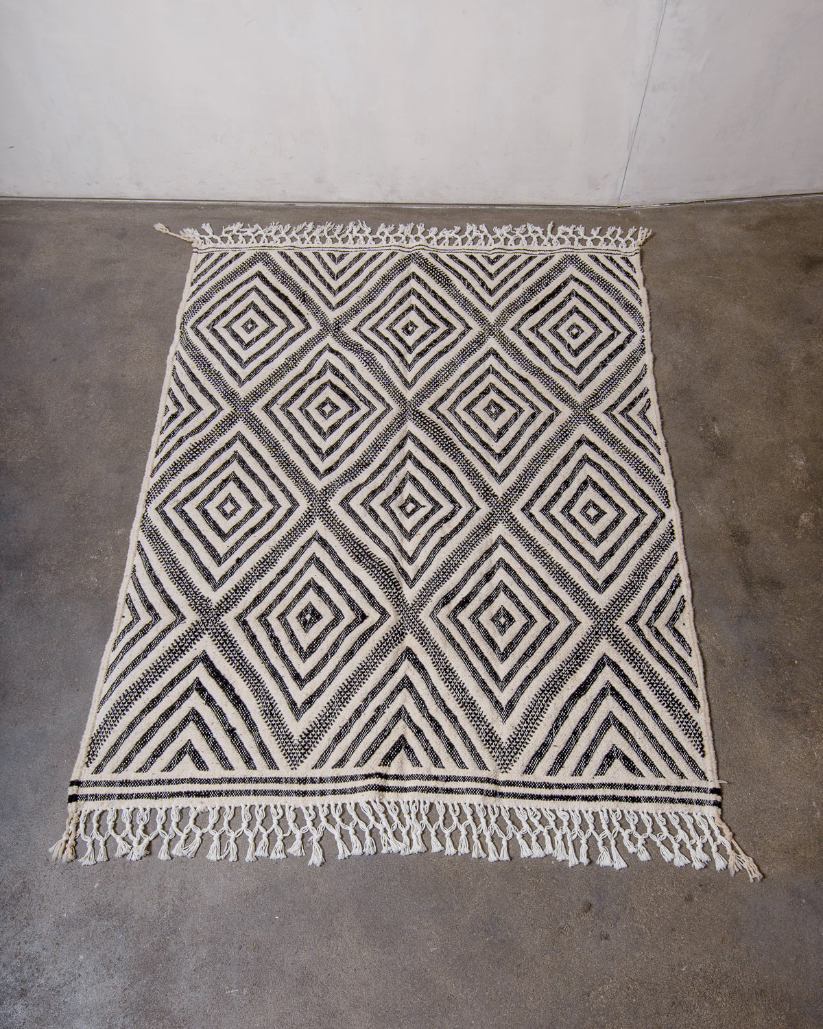 Berberlin Kelim rug with black and white diamond pattern, laying flat on concrete floor.